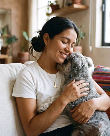 Mujer abrazando a su perro schnauzer, con un dije dorado de perro